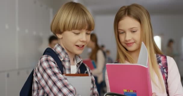 Κοντινό πλάνο του κομψού Καυκάσου έφηβου αγοριού και κοριτσιού που στέκονται στο σχολείο με τα βιβλία και τα βιβλία τους για το επόμενο μάθημα. — Αρχείο Βίντεο
