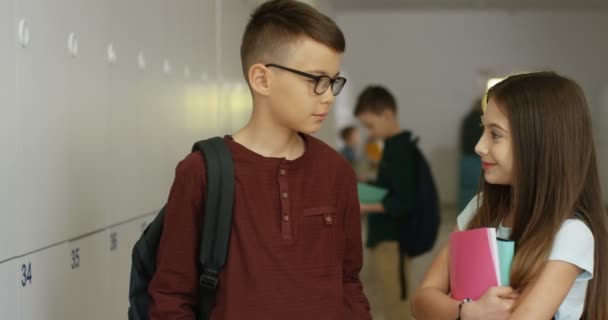Портрет дружелюбных учеников, подростка и школьницы, смотрящих друг на друга и улыбающихся в камеру в коридоре. — стоковое видео