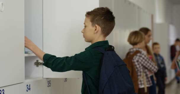 Hvid teenager lærd tager ud lærebøger fra hans skab og derefter smiler til kameraet på skolens korridor. Portrætbillede. – Stock-video