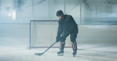 Beyaz tenli yakışıklı, konsantre erkek hokey oyuncusunun portresi. Üniformalı ve kasklı. Buz arenasında kulüp ve diskle duruyor. Buzlu yüzeyinde sopası ve diski olan sporcu. Kaleci..