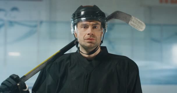 Ritratto di giovane e affascinante giocatore di hockey maschile caucasico in casco e con club che guarda la macchina fotografica sull'arena di ghiaccio. Primo piano di attraente sportivo in botte con bastone. — Video Stock