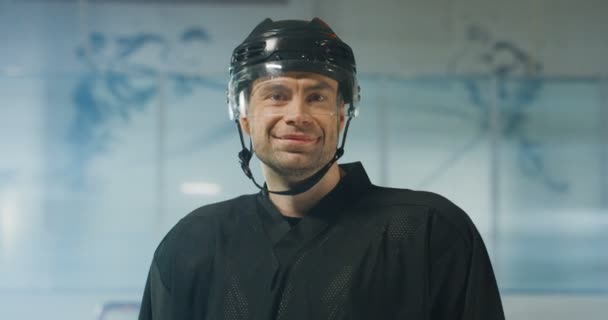 Ritratto di giovane giovane hockey caucasico felice in casco e con il club che sorride alla telecamera sull'arena di ghiaccio. Primo piano di allegro sportivo attraente in botte con bastone. — Video Stock