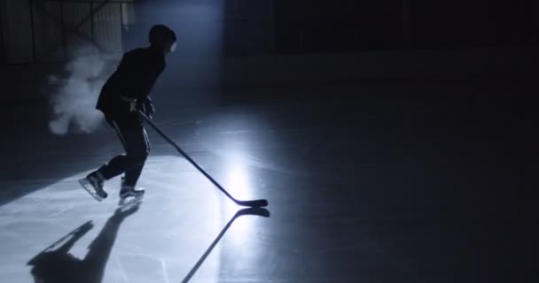 Tmavá silueta mužského hokejisty v uniformě, bruslařů a helmy klouzající rychle na ledové aréně a bít puch s holí během hry. Sportovec s kyjem hity disk na ledě.