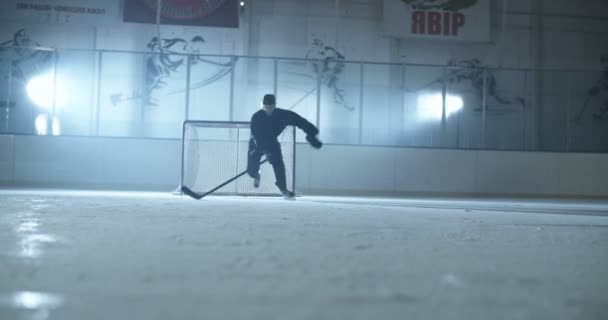 Běloch mužský hokejista v casque, uniformě a s klubem bruslení rychle na ledové aréně od brány ke kameře. Sportovec v helmě klouzání na ledu s tyčí. — Stock video