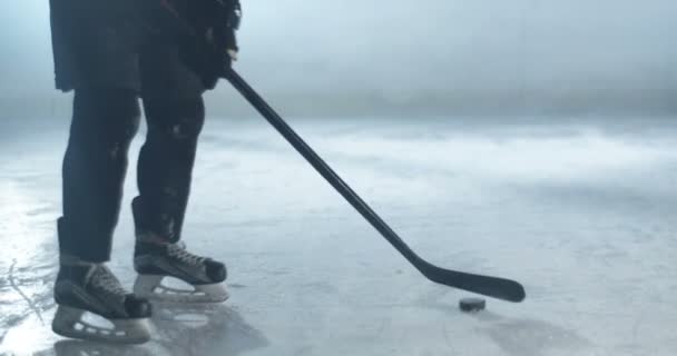 Retrato filmado de branco jovem jogador de hóquei masculino em uniforme, casco e em patinadores de pé no gelo e jogando com clube e disco no gelo. Treinamento de desportista com pau e disco na arena gelada. — Vídeo de Stock