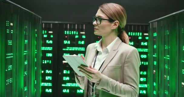 Mujer hermosa joven caucásica en gafas caminando en servidores con dispositivo de tableta, tocando y comprobando procesadores de big data. Analítica femenina en el almacenamiento de datos trabajando en la seguridad digital de la base de datos. — Vídeo de stock