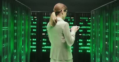 Kafkasyalı, gözlüklü, tablet cihazıyla sunucularda yürüyen, büyük verileri takip eden genç bir kadın. Veri depolamada kadın analitiği üzerine arka plan Veritabanının dijital güvenliği üzerinde çalışıyor.