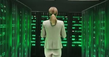 Tabletli beyaz bir kadının arkasında büyük veri bilgileriyle sunucular arasında yürüyordu. Veritabanı deposunda çalışan yeşil işlemciler. Dijital telekomünikasyon kadın çalışanının arka planı.