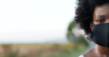 Spor yaptıktan ya da koştuktan sonra kameraya bakan maskeli Afro-Amerikan terli kadın sporcunun yüzünün yarısını kapatın. Açık havada koşan kadın sporcunun portresi.