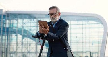 Gözlüklü son sınıf öğrencisi caddede bisiklete biniyor ve büyük cam modern binadaki tablet cihazını tıklatıyor ya da kaydırıyor. Yaşlı büyükbaba alet bilgisayarı kullanıyor ve açık havada geziniyor..