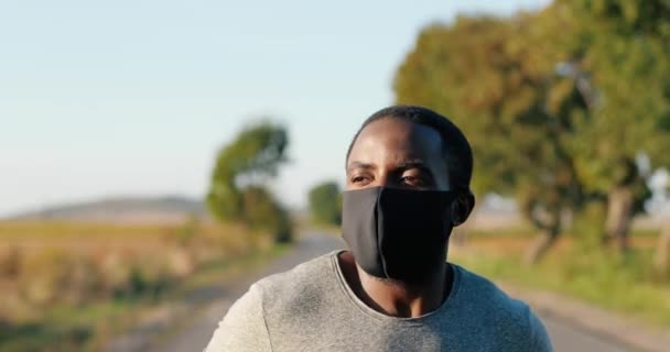 Close-up van Afro-Amerikaanse knappe sterke mannelijke jogger die op zomerdag op het platteland rondrent. Aantrekkelijke sportieve man met masker die buiten jogt. Pandemisch concept. — Stockvideo