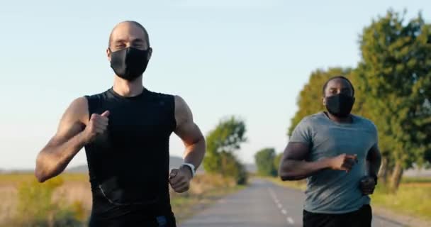 Белый и африканский американец красивый сильный мужчина бегает трусцой по сельской местности в летний день. Привлекательные спортсмены смешанных рас бегают в масках. Пандемия. Конкуренция. — стоковое видео