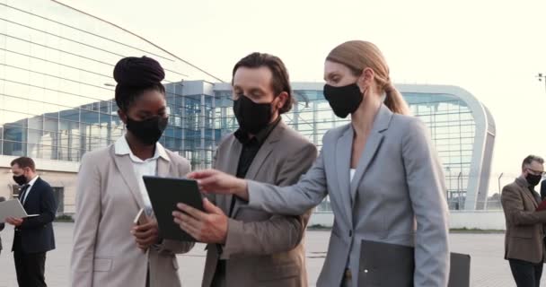 Mixed-races young male and females business partners in masks talking and using tablet device outdoor at street. Businessman and businesswomen having conversation in city. Pandemic coronavirus. — Stock Video