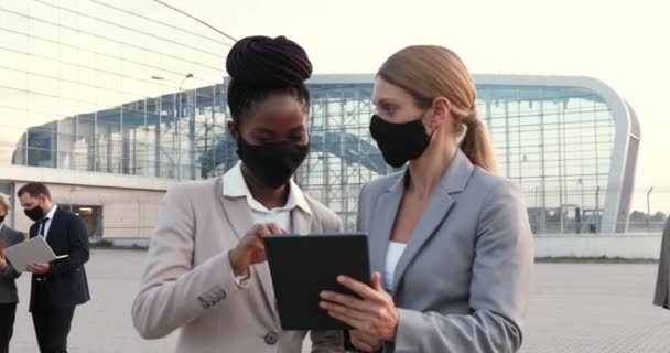 Mixed-races jonge vrouwen zakenpartners in maskers praten en het gebruik van tablet apparaat buiten op straat. Multi-etnische zakenvrouwen in gesprek in de stad. Pandemisch coronavirus. Vrouwelijke collega 's. — Stockvideo