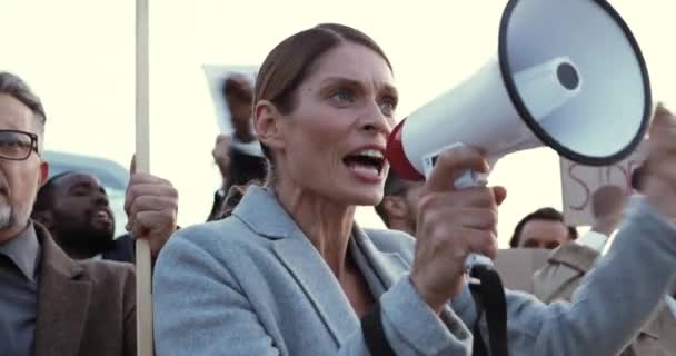 Close up de empresária caucasiana falando em megafone ao ar livre em protesto contra o desemprego em multiétnica multidão. Mulher tendo discurso em greve contra a desigualdade. Manifestantes durante crise. — Vídeo de Stock