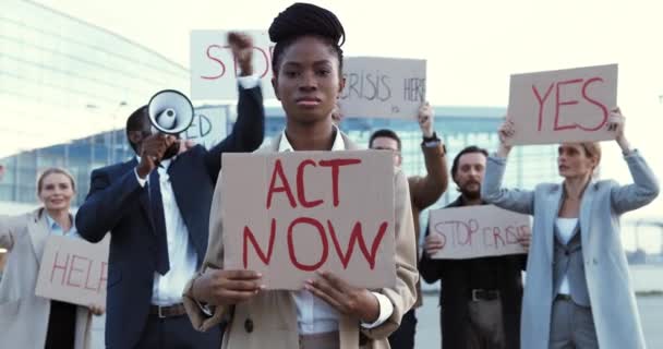 Portret van een Afro-Amerikaanse vrouw die buiten staat te protesteren met poster Act Now. Mooie vrouwelijke demonstrant in staking tegen werkloosheid. Mixed-races mensen op de achtergrond. Protesteren. Opvallend. — Stockvideo