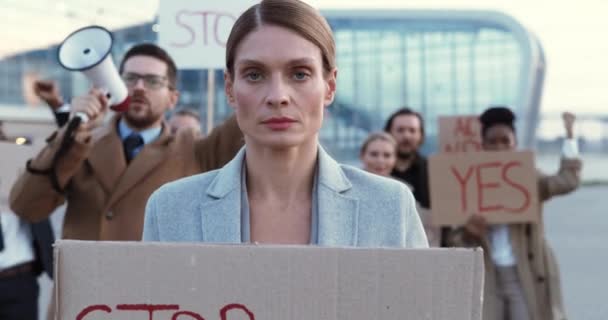 Portret van een blanke vrouw die buiten staat te protesteren met poster Stop Crisis. Mooie vrouwelijke demonstrant in staking tegen werkloosheid. Mixed-races mensen op de achtergrond. Protesteren. Opvallend. — Stockvideo