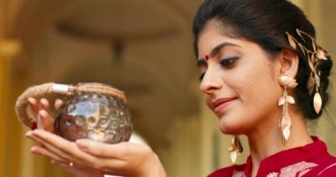 Alnında nokta olan ve geleneksel kırmızı giysileri olan Hindu genç ve güzel bir kadın bina önünde kameraya gülümsüyor ve içinde mum olan lambayı tutuyor. Kültür ve gümrük kavramı.