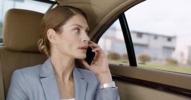 Pahalı bir arabanın arka koltuğunda oturan ve cep telefonuyla konuşan güzel, beyaz bir kadını yakından çek. Başarılı bir iş kadını cep telefonuyla konuşuyor. Telefonla ara. İş görüşmesi.