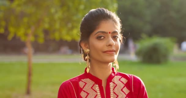 Retrato de jovem hindu bela mulher com ponto na testa e na roupa tradicional sorrindo para câmera alegremente. Ao ar livre no parque. Close up de menina feliz muito sorriu da Índia sob a luz do sol. — Vídeo de Stock