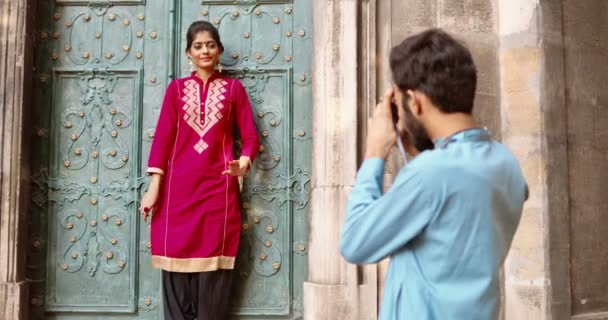Hinten auf einem männlichen Fotografen, der ein Foto der hinduistischen jungen schönen Frau in traditionellem Outfit macht. Das Heck des Menschen. Weibliches hübsches Model posiert vor der Kamera an der antiken Tür. Draußen. Fotografieren. Fotos. — Stockvideo
