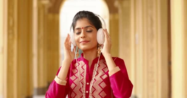 Hindoe jonge gelukkige mooie vrouw met rode stip op het voorhoofd en in traditionele kleren luisteren naar muziek in hoofdtelefoon buiten. Vrij glimlachte vrolijke vrouw genieten van favoriete lied. — Stockvideo