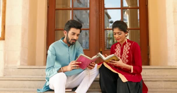 Hindoe paar man en vrouw zitten op stappen buiten, praten en lezen van boeken. Mannelijke en vrouwelijke studenten in traditionele kleding lezen leerboeken en studeren samen. Studeren met handboeken in India. — Stockvideo