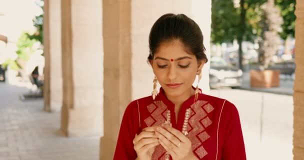 Mujer hermosa joven hindú con punto rojo en la frente y en traje tradicional oliendo perfume al aire libre. Elegante encantadora hembra olfateando aroma y aroma en la calle. Concepto de belleza. Perfume. — Vídeos de Stock