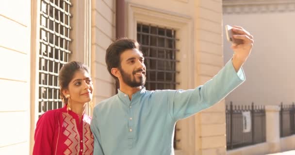 Hinduistka s tečkami na čele a muž v turbanu stojí venku a fotí selfie na smartphonu. Muž a žena se usmívají a fotí selfie na mobilním telefonu. Turisté. Kultura. — Stock video