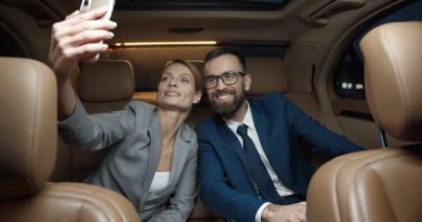 Kafkasyalı genç işadamı ve iş kadını arabanın arka koltuğunda oturmuş akıllı telefon kamerasıyla selfie çekiyorlar. Birkaç iş ortağı neşeyle gülümsüyor ve cep telefonuyla fotoğraf çekiyor.