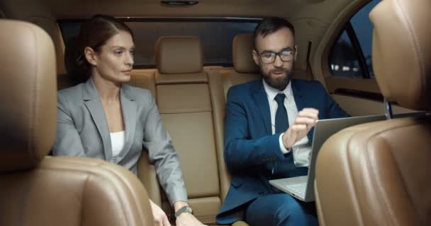 Beyaz, genç bir çift iş ortağı pahalı bir arabanın arka koltuğunda otururken anlaşma yapıyor ve sözleşme imzalıyor. İş adamı ve işkadını el sıkışıyorlar. Dizüstü bilgisayarda çalış. — Stok video