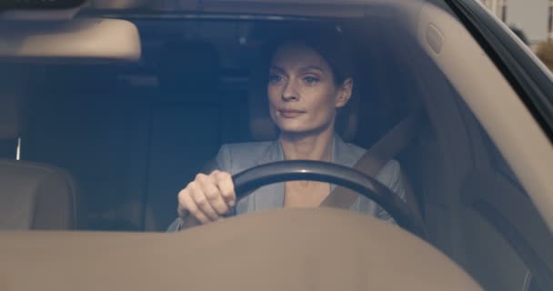 Vista através do pára-brisas. Bonita mulher de negócios caucasiana jovem sentado no volante, usando cinto de segurança e condução de carro caro. Motorista feminina atraente. — Vídeo de Stock