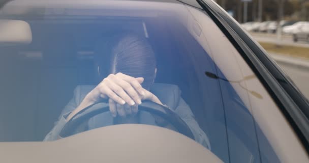 Junge kaukasische schöne gestresste Frau in Depression sitzt im Auto am Steuer und lehnt sich kopfüber darauf. Attraktive, traurige Autofahrerin. Verärgerte Geschäftsfrau. Durch Windschutzscheibe. — Stockvideo