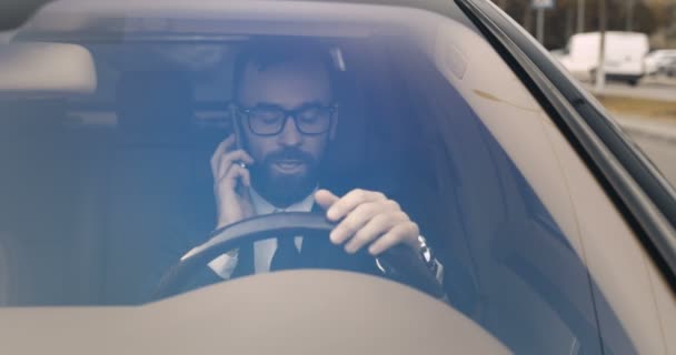 Caucasico arrabbiato uomo d'affari stressato seduto al volante e parlando sul cellulare. Autista maschio urla sul telefono cellulare e termina la conversazione con rabbia. Vista attraverso il parabrezza. Problematiche. — Video Stock