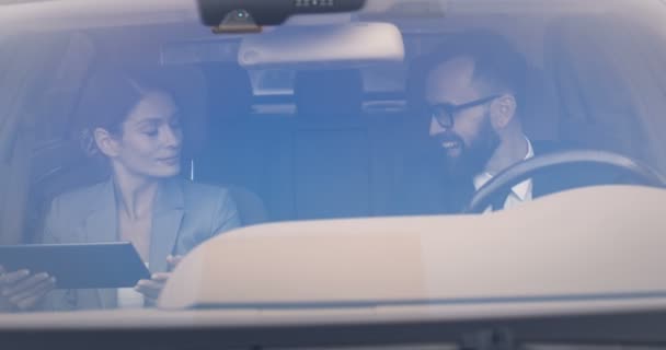 Fröhlich fröhliche kaukasische Frau und Mann fahren frühmorgens zur Arbeit und reden. Mann am Steuer und Frau mit Tablet-Gerät, Nachrichten online lesen. Paar von Geschäftspartnern im Automobilbereich. — Stockvideo