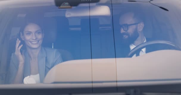 Feliz esposa y marido caucásicos alegres que conducen temprano en la mañana para trabajar y reír. Hombre conduciendo y mujer usando móvil, bebiendo café. Un par de colegas de negocios en el automóvil. Bebida para sorber — Vídeo de stock