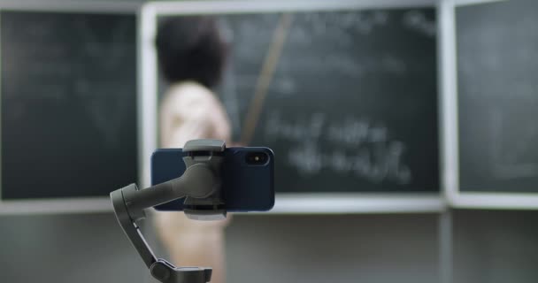 学校でのスマートフォン録画ビデオレッスン。オンライン学習。アフリカ系アメリカ人の若い女性教師が授業で数学や物理式を説明する。隔離の概念。コロナウイルスの研究. — ストック動画