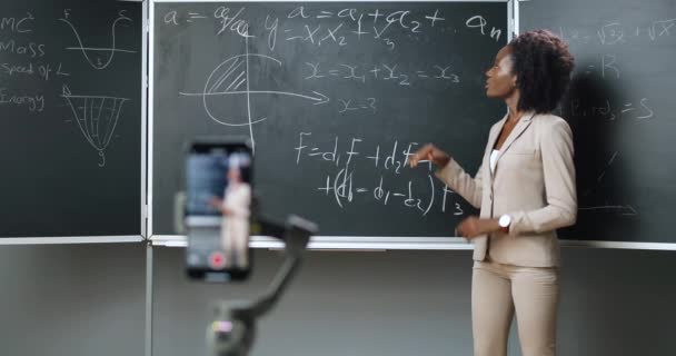 Okulda akıllı telefon kayıt videosu dersi. Çevrimiçi çalışma. Sınıfta matematik ya da fizik formüllerini açıklayan Afrikalı genç bayan öğretmen. Karantina konsepti. İnternetle çalış. Tecrit. — Stok video