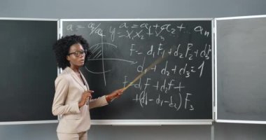 Sınıfta gözlüklü genç Afrikalı Amerikalı kadın öğretmen fizik ya da geometri kanunlarını sınıfa anlatıyor. Öğretmenlik konsepti. Okul çevrimiçi. Eğitici bir ders. Matematik dersi.