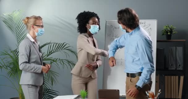 Καυκάσιοι Αφροαμερικανοί και άντρες με ιατρικές μάσκες που αγγίζουν τους αγκώνες όπως χαιρετισμός ή συμφωνία. Πανδημία. Επιχειρηματίας μικτών φυλών και γυναίκες επιχειρηματίες στο γραφείο. Πολυεθνική. — Αρχείο Βίντεο