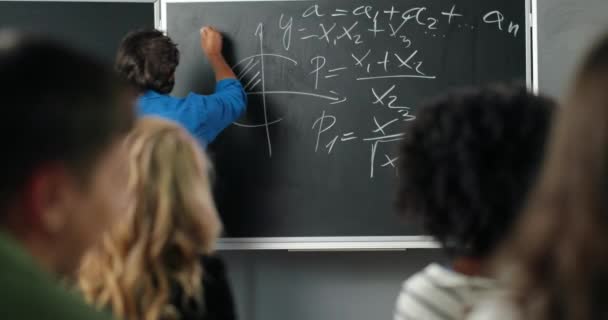 Hinten auf einem kaukasischen männlichen Lehrer, der im Klassenzimmer Mathe-Gesetze und Formeln an die Tafel schreibt. Rückenansicht eines Dozenten, der Studenten Mathematik oder Physik erklärt. Universitätsstudie. — Stockvideo