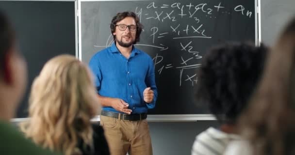 Homem branco professor de óculos na escola em quadro-negro conversando com alunos ou alunos. Conceito de aula de matemática. Professor do sexo masculino explicando as leis da matemática na aula. Conceito de educação. — Vídeo de Stock