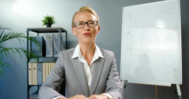 Kaukasiska snygg kvinna i glasögon sitter på kontoret och prata med kameran och utbilda företag. Kvinnlig coach inspelning video blogg. Blogger Affärskvinna coaching online. — Stockvideo