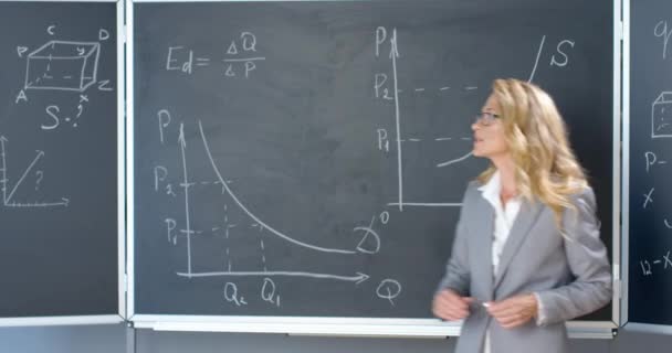 Vrouwelijke blanke leraar met een bril op schoolbord en uitleg over formules en wiskunde wetten. Mooie vrouw die les geeft in wiskunde of natuurkunde. Lezing op school of hogeschool. — Stockvideo