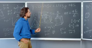 Beyaz tenli yakışıklı erkek öğretmen formüller, grafikler ve yasalarla tahtada duruyor ve işaretleyici ile açıklıyor. Okulda ya da üniversitede matematik öğretmeni. Matematik dersi.