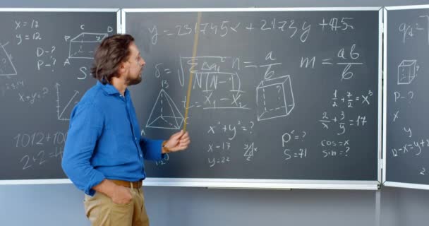 Caucasiano bom olhar professor do sexo masculino em pé no quadro negro com fórmulas, gráficos e leis e explicando com ponteiro. Professor de matemática na escola ou faculdade. Leitura matemática. — Vídeo de Stock