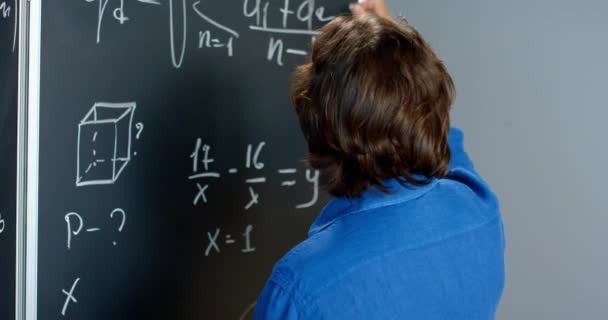 Bakåt syn på kaukasiska manliga föreläsare skriva matematik eller fysik formler med kritor på svarta tavlan. Portrair av manlig lärare som arbetar i skolan och tittar till kameran. Matematikens lärdom. Bakre delen. — Stockvideo