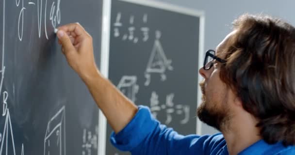 Primer plano del profesor varón caucásico escribiendo fórmulas matemáticas o físicas con tiza en pizarra. Hombre profesor trabajando en la escuela. Lección de matemáticas. Matemático. — Vídeo de stock