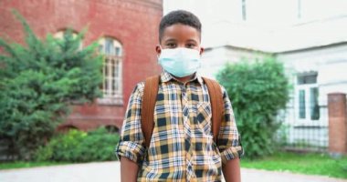 Okul bahçesinde maske takmış şirin, mutlu, Afro-Amerikan bir çocuğun portresi. Karantinadan sonra okul çantasıyla dışarıda duran liseli erkek öğrenci. Salgın sırasında çalış. Öğrenci konsepti