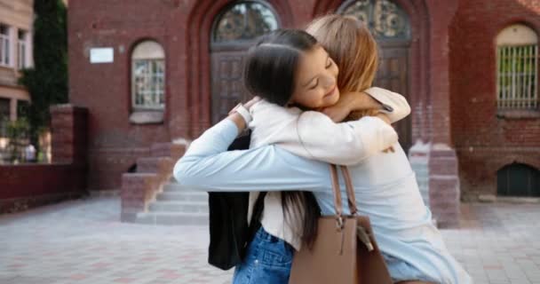 Schöne fröhliche Kaukasierin, die sich vor dem Unterricht auf dem Schulhof mit einem kleinen süßen Teenie-Mädchen umarmt. Porträt einer fröhlichen hübschen Schülerin umarmt ihre Mutter und rennt zur Schule — Stockvideo